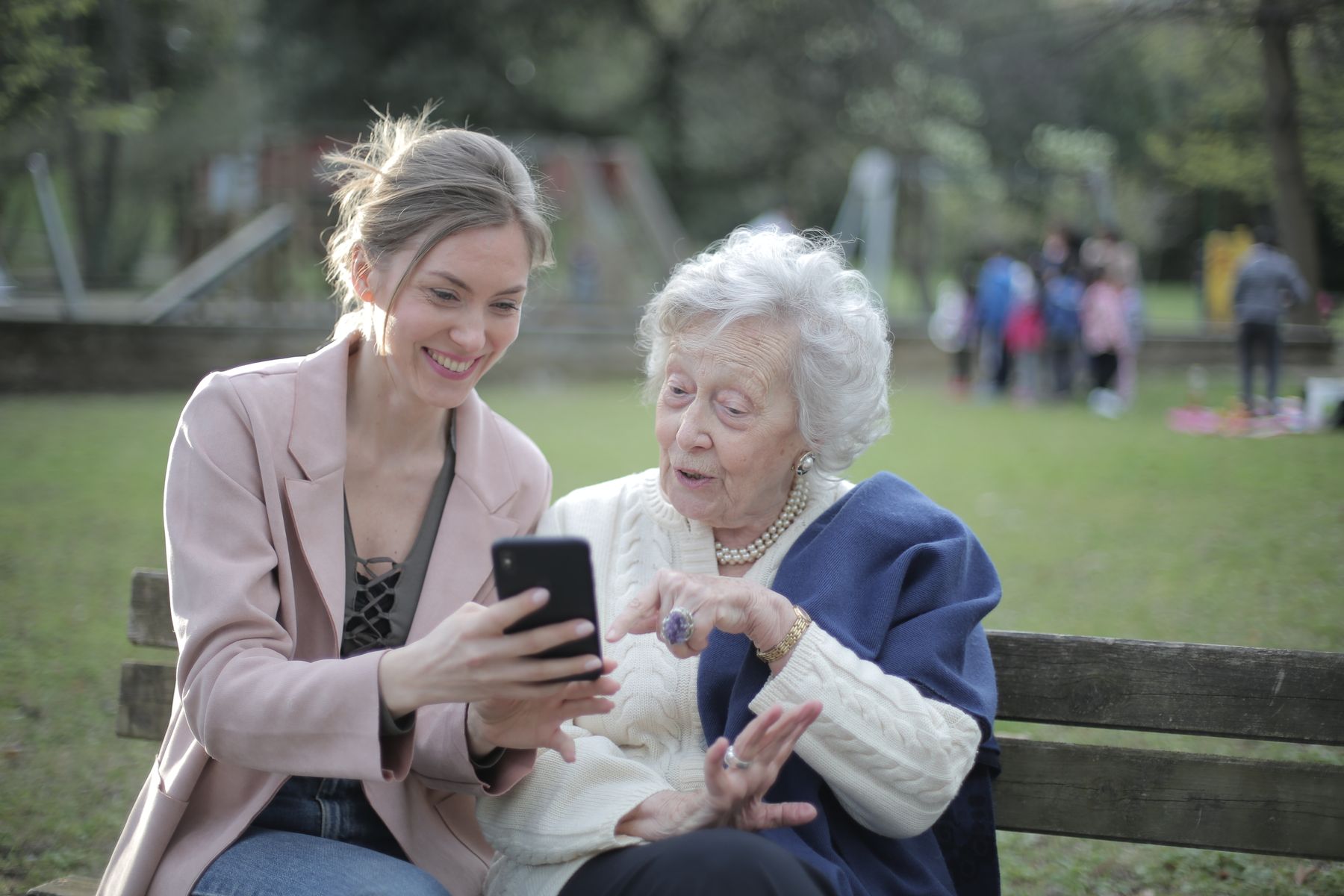 An adult daughter and her senior mother looking at a smartphone together in a park
